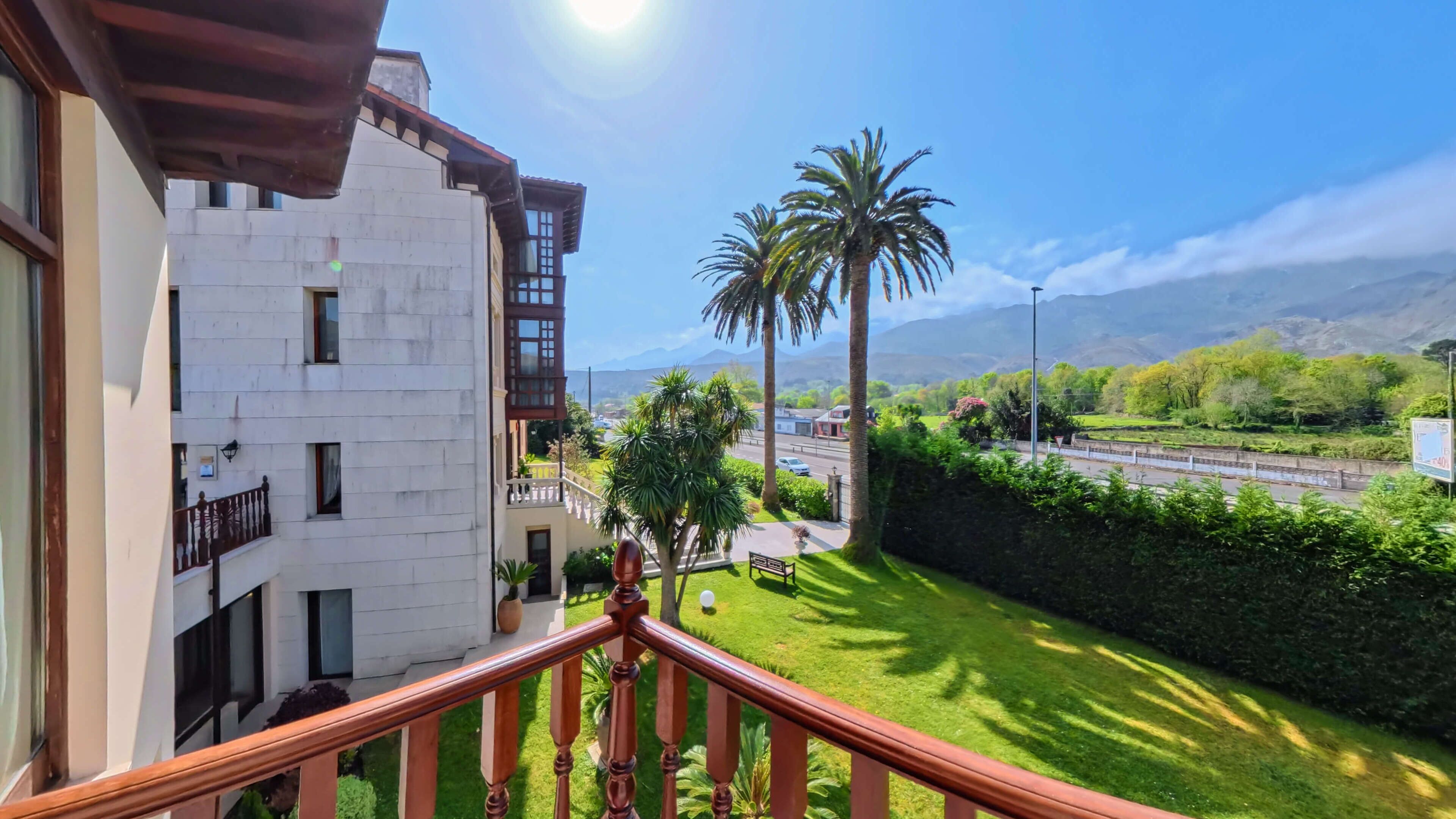 Un balcón con vistas a un jardín verde, palmeras y una carretera con coches.