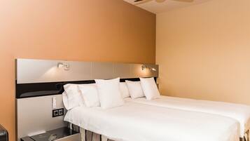 Habitación de hotel con cama, mesita de noche, ventilador de techo y lámpara fijada a la pared.
