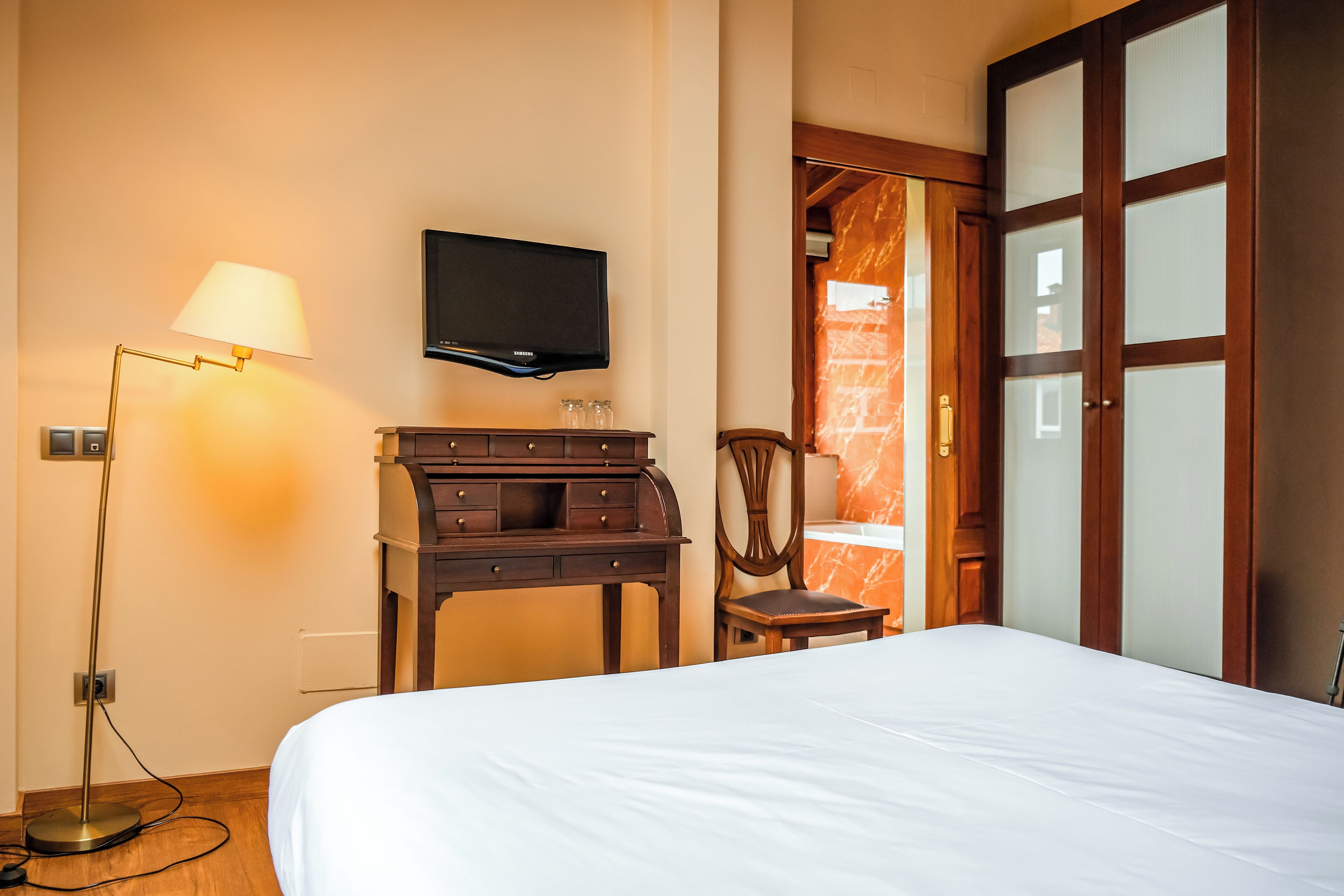Una habitación de hotel con cama, escritorio, silla, televisor y armario.