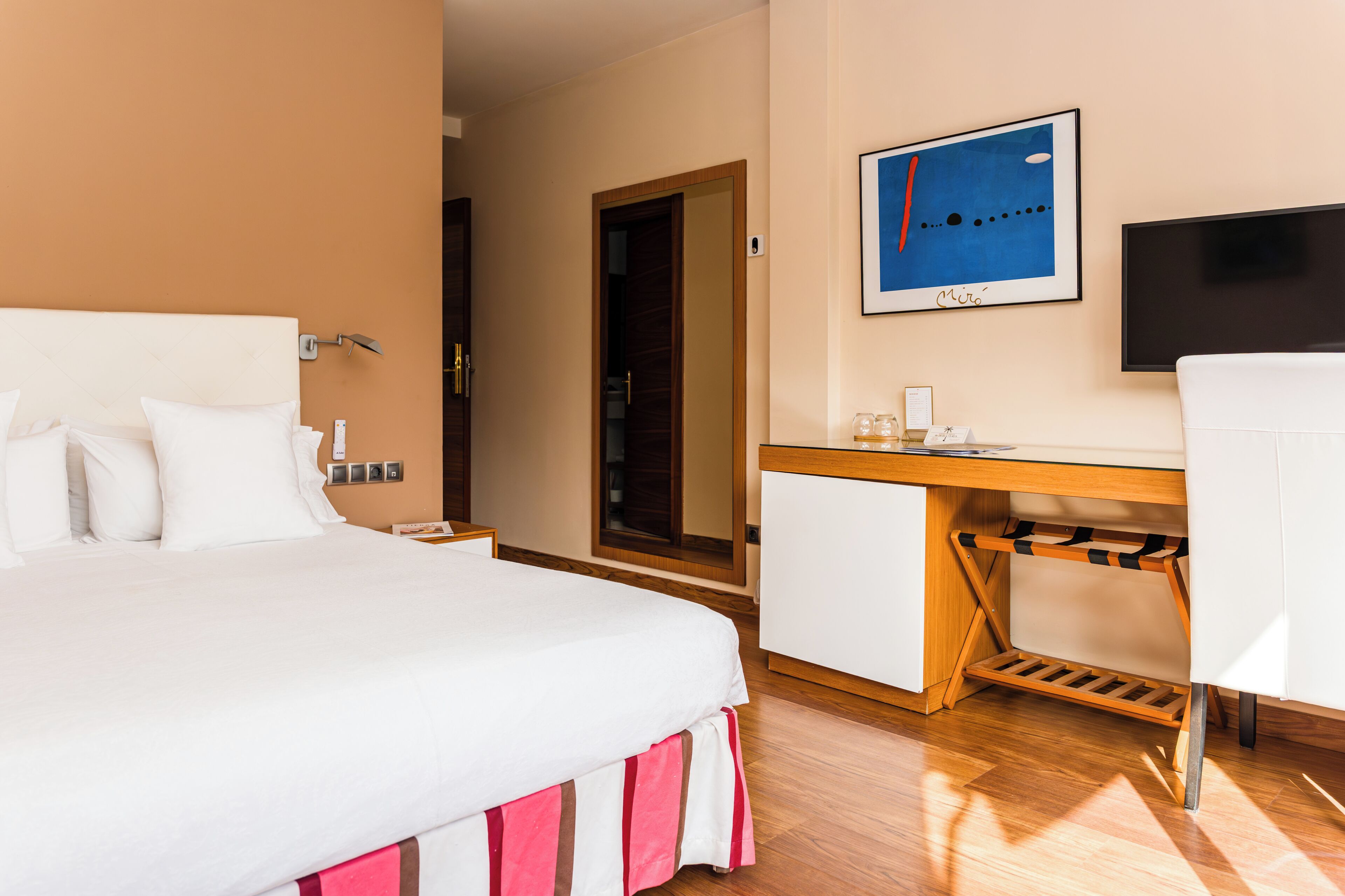 A hotel room with a bed, a desk, a chair, a TV, and a mirror.