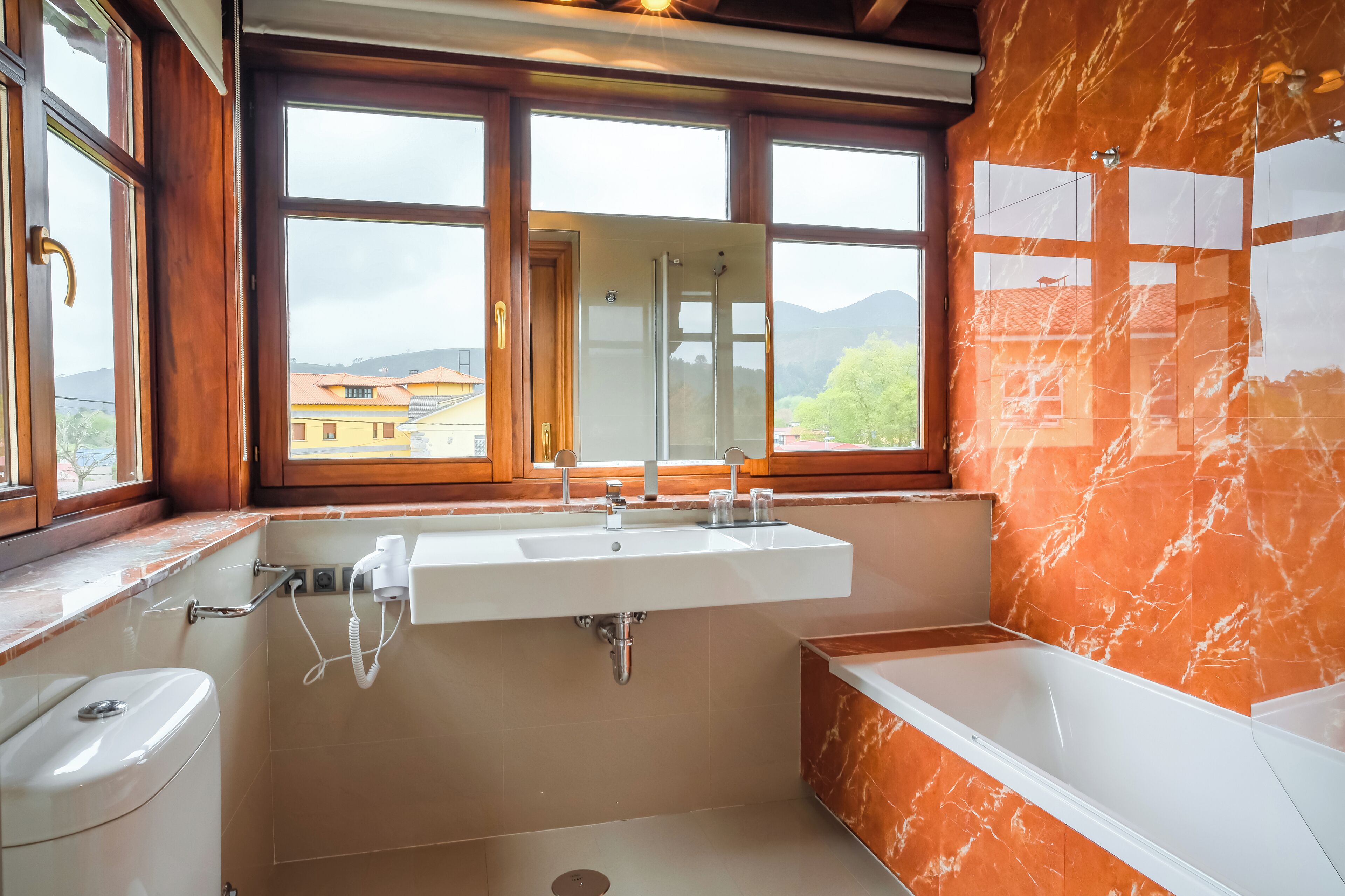Un baño con un ventanal grande, un lavamanos, un inodoro y una bañera.