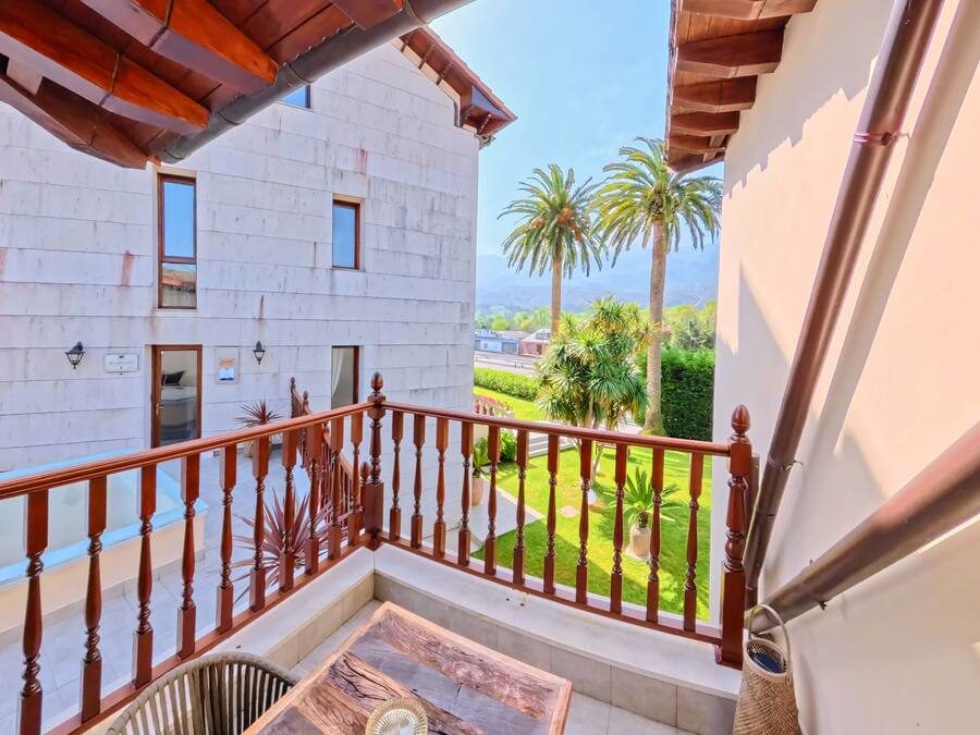 Un balcón con baranda de madera, una mesa pequeña y vistas a un edificio con muchas ventanas y un jardín.
