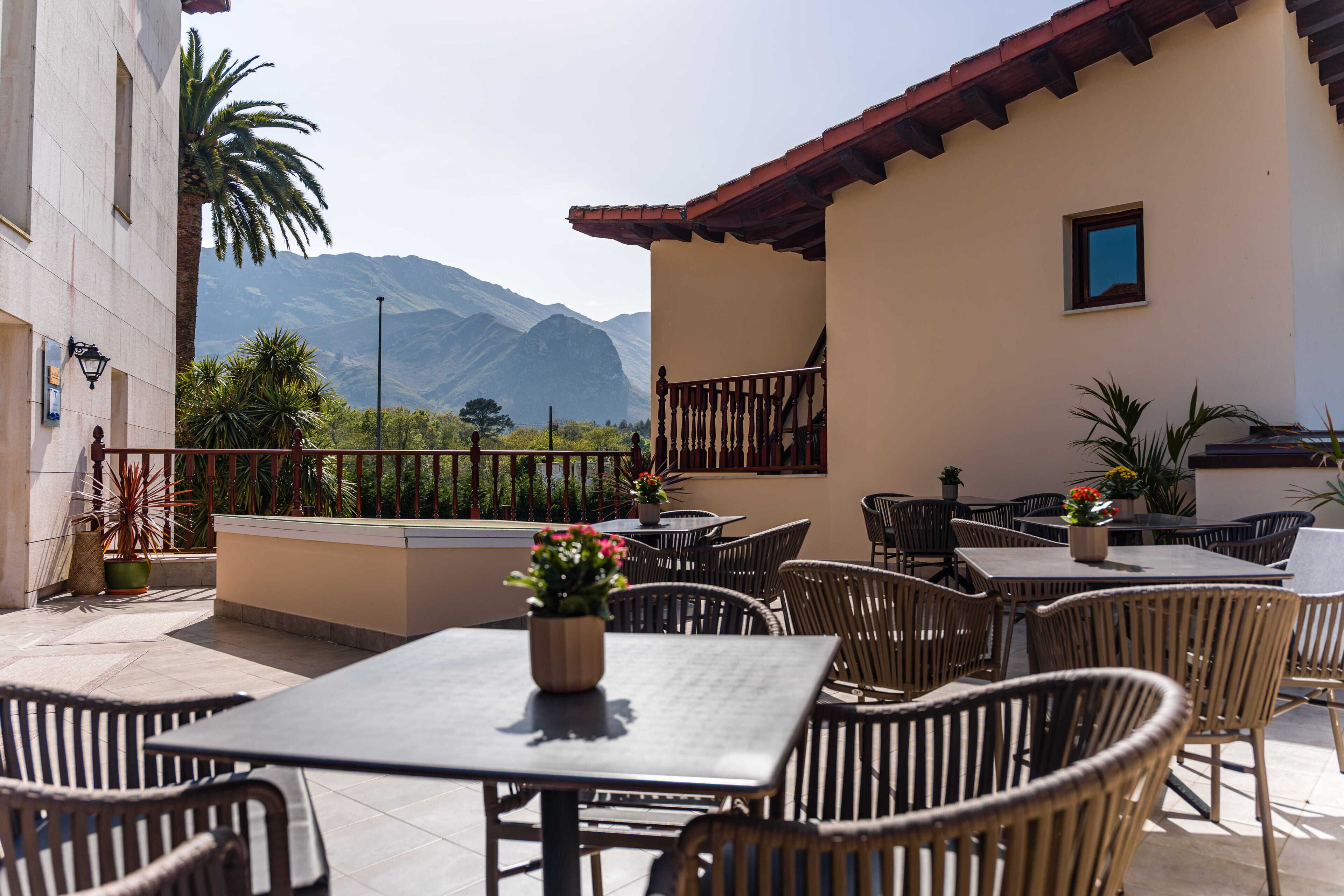 An outdoor patio with tables and chairs, a view of mountains, and a building with a tiled roof.