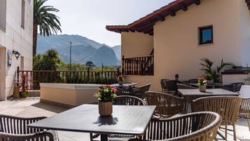 An outdoor patio with tables and chairs, a view of mountains, and a building with a tiled roof.