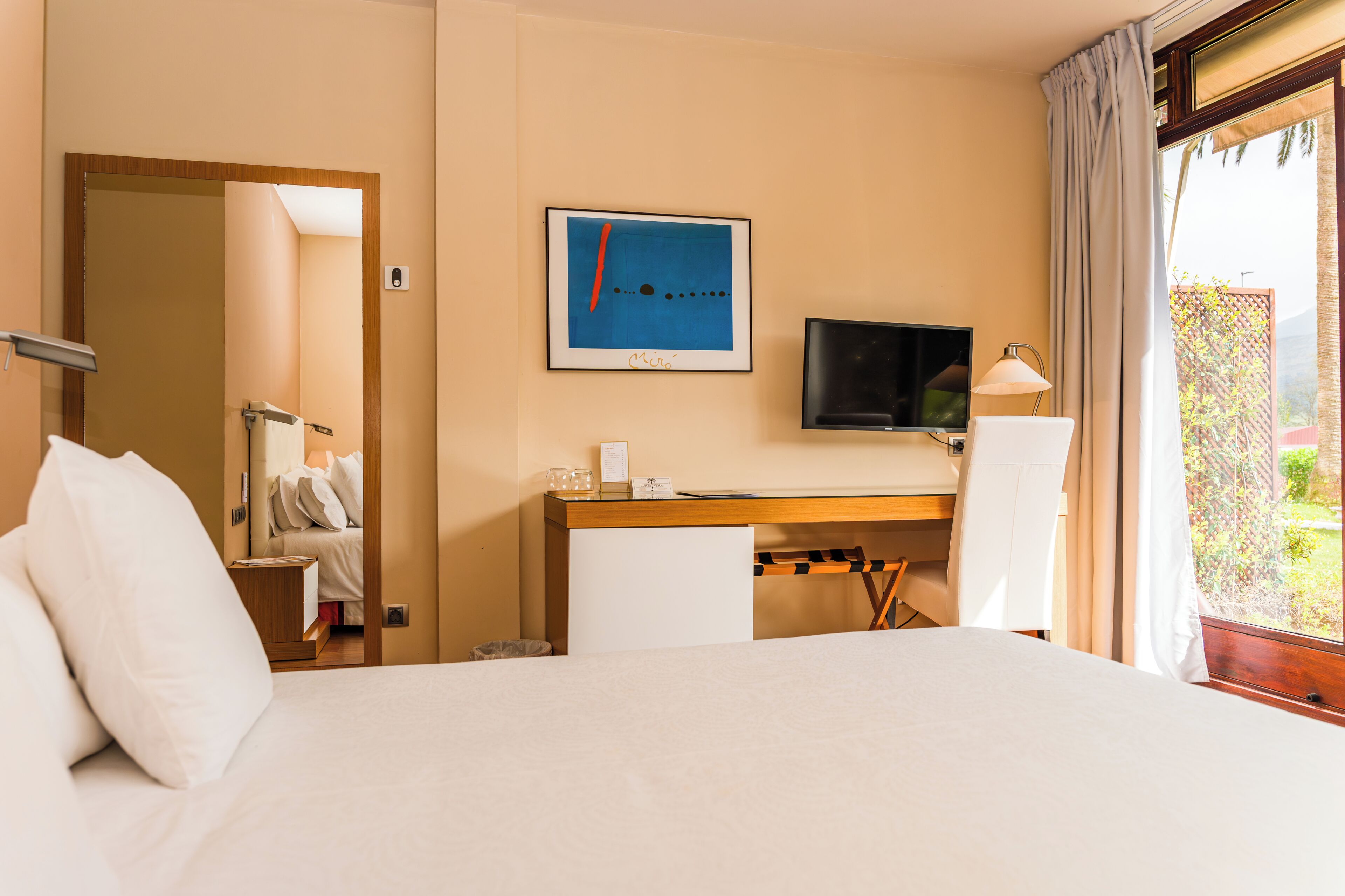 A hotel room with a bed, desk, chair, TV, and a window with curtains.