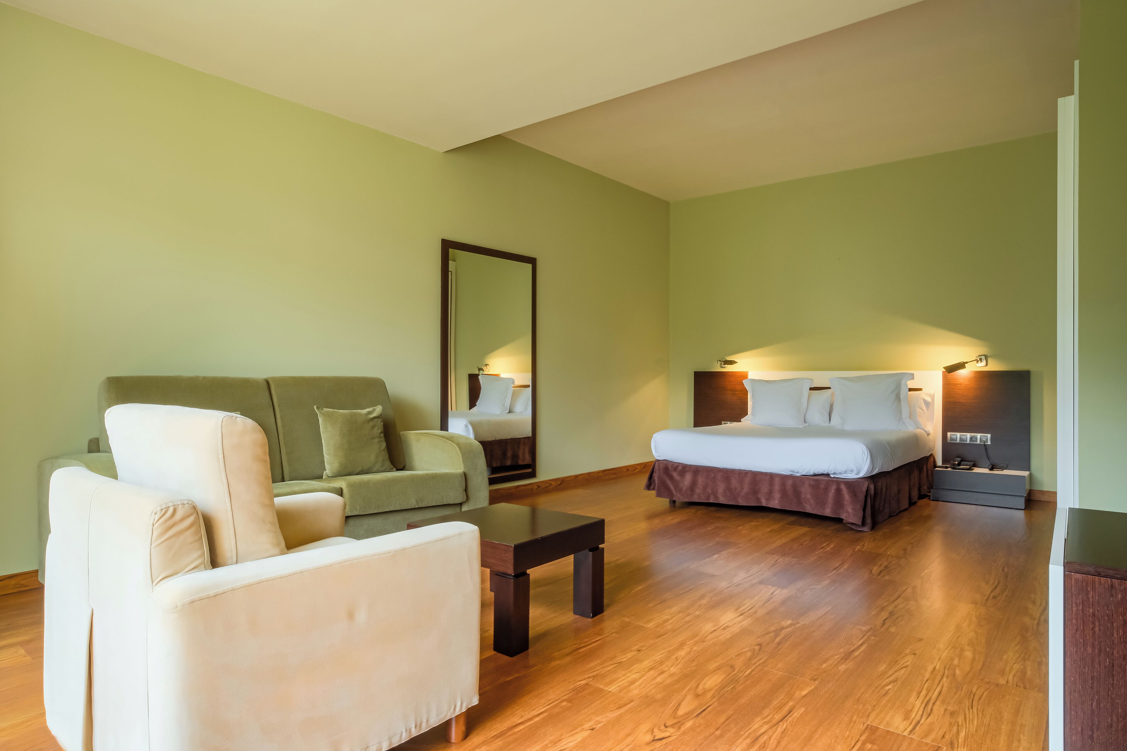 Una habitación de hotel con cama, sofá, sillón, una mesita pequeña y una mesita de noche.