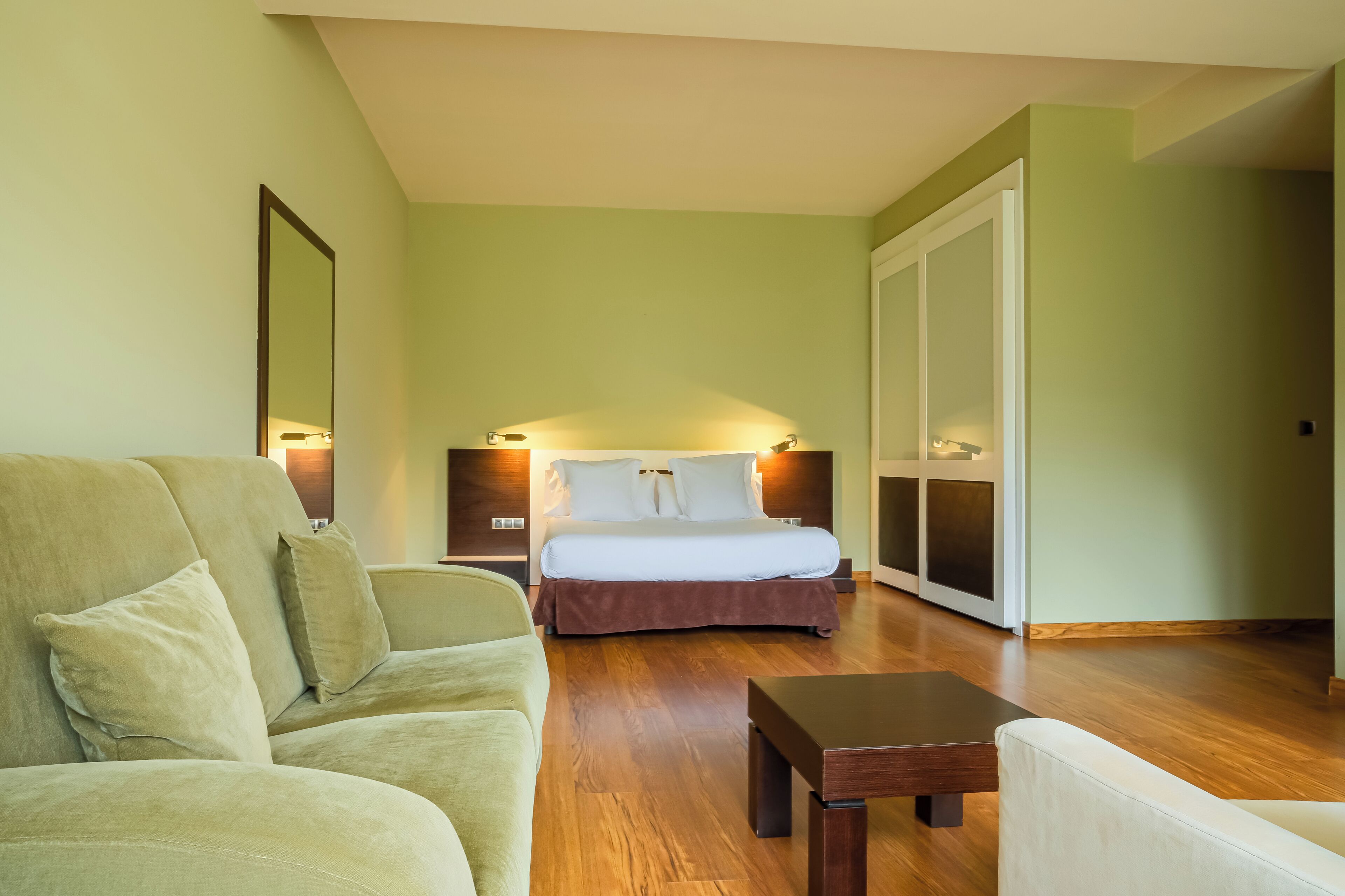 Una habitación de hotel con cama, sofá, mesa de madera y un espejo grande.