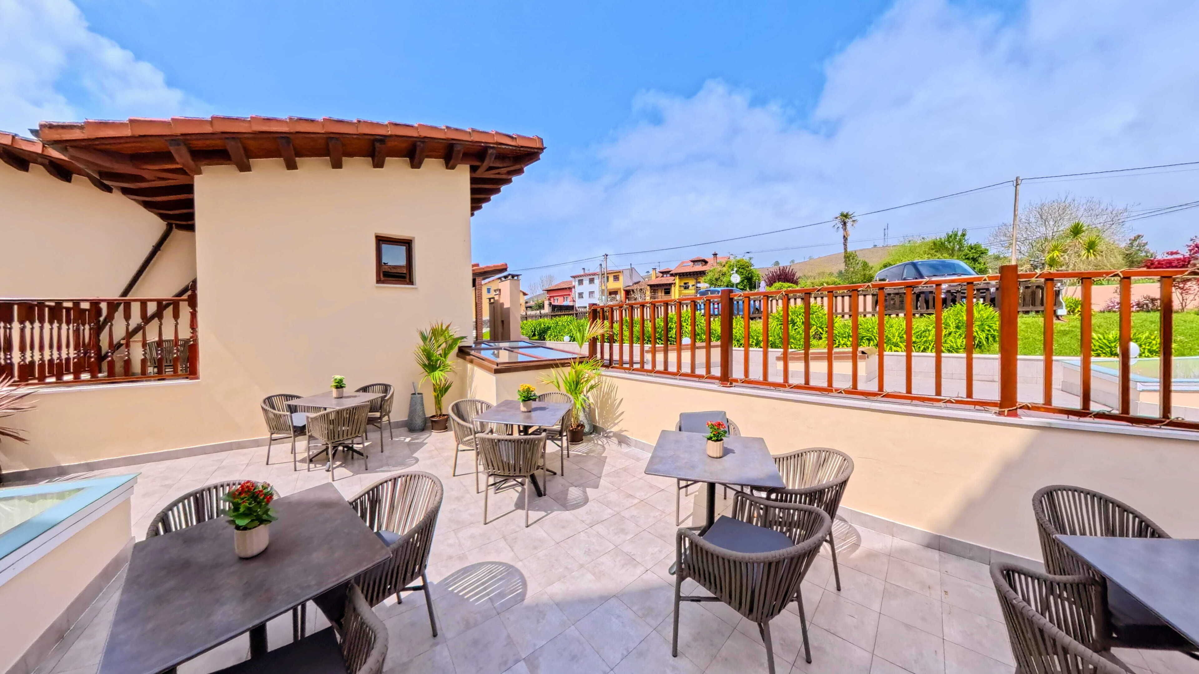 Terraza en la azotea con mesas al aire libre, cerramiento de vidrio y vistas a una zona residencial.