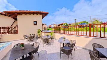 Terraza en la azotea con mesas al aire libre, cerramiento de vidrio y vistas a una zona residencial.