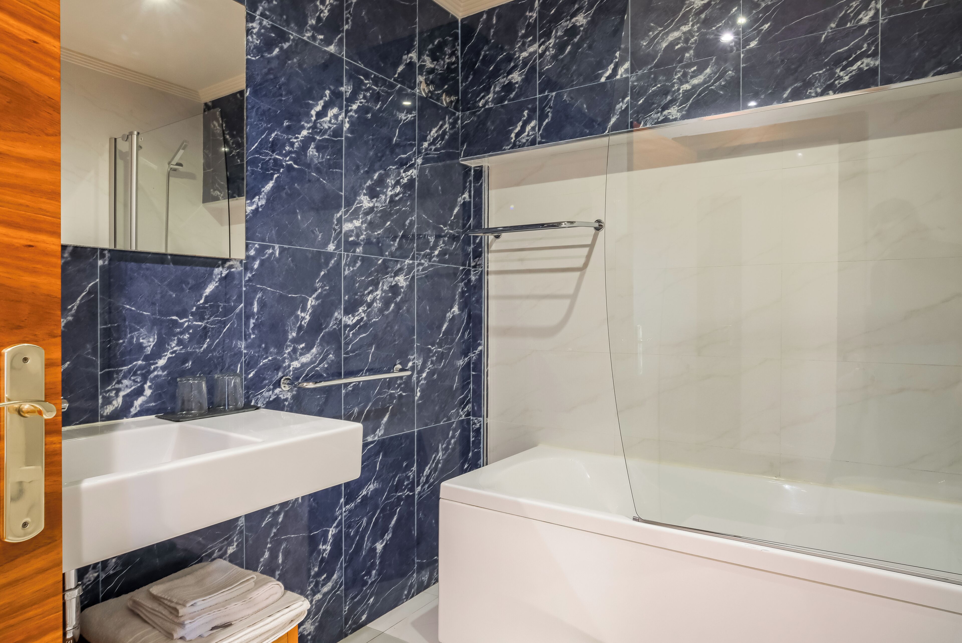 Un baño moderno con salpicadero de mármol, ducha con mampara de cristal, lavabo blanco y bañera.
