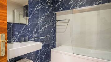 Un baño moderno con salpicadero de mármol, ducha con mampara de cristal, lavabo blanco y bañera.