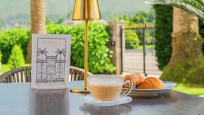 A table with a glass cup of tea, a plate of croissants, a gold lamp, and a brochure for Indiana Boutique Hotel. - Indiana Boutique Hotel (Llanes)
