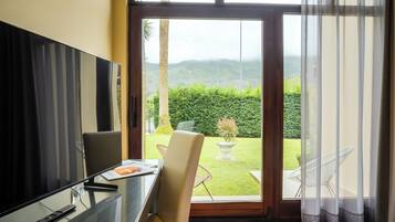Una habitación con puerta de cristal que da a un jardín, un televisor a la izquierda y una mesa con sillas.