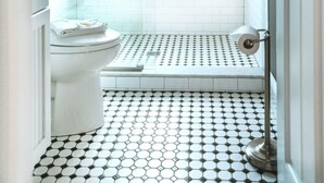A bathroom with a white toilet, a window, a shower, and a patterned floor. - Bright Queen Room with Fireplace & Skylight - Steps from Downtown Provincetown (Provincetown)