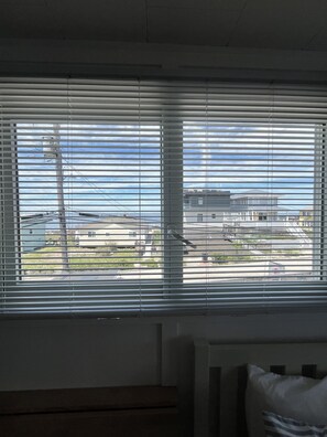 Ein Zimmer mit Fenster, Rollläden, einem Bett mit Kopfkissen und einem Heizkörper.