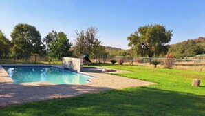 Una piscina con borde de baldosas, rodeada de césped y árboles.