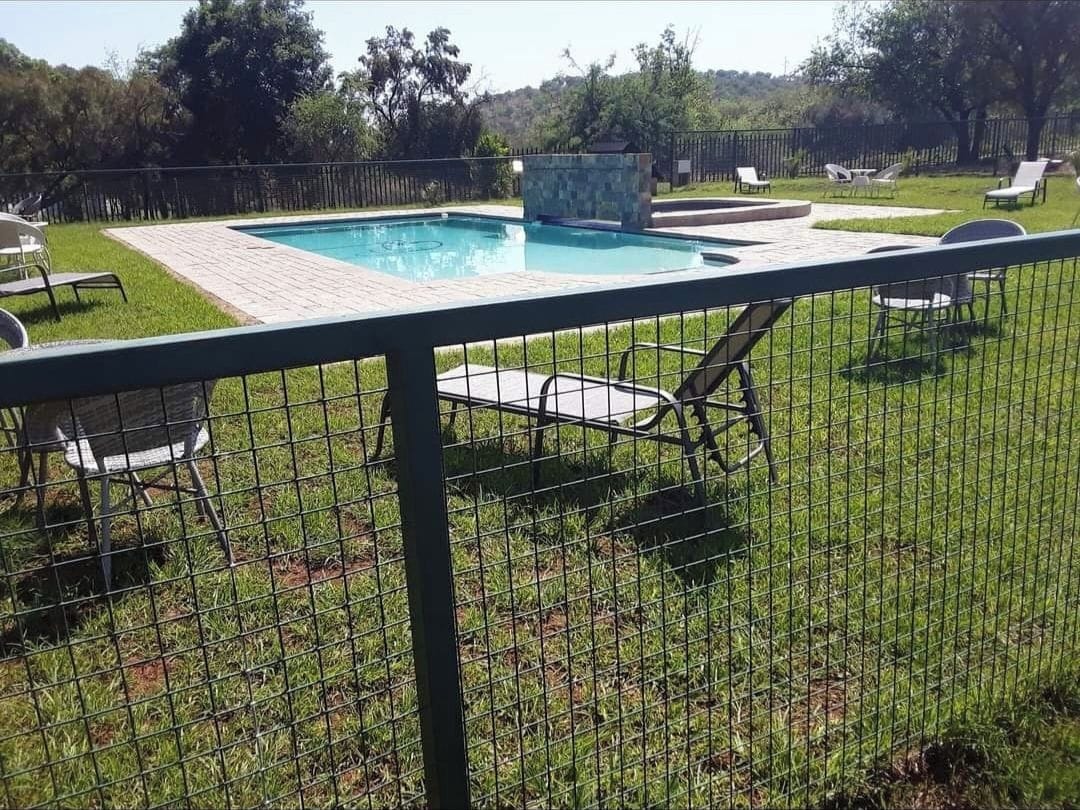 A fenced backyard with a swimming pool, lounge chairs, and a stone feature.