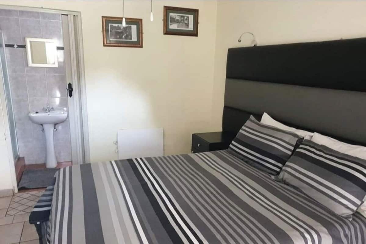 A bedroom with a bed, a bedside table, a nightstand, a window, and a door leading to a bathroom.
