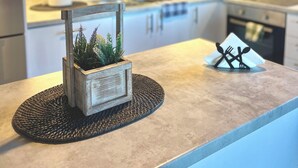 Una cucina con mobili bianchi, un'isola in legno con una pianta e un sottopentola intrecciato.