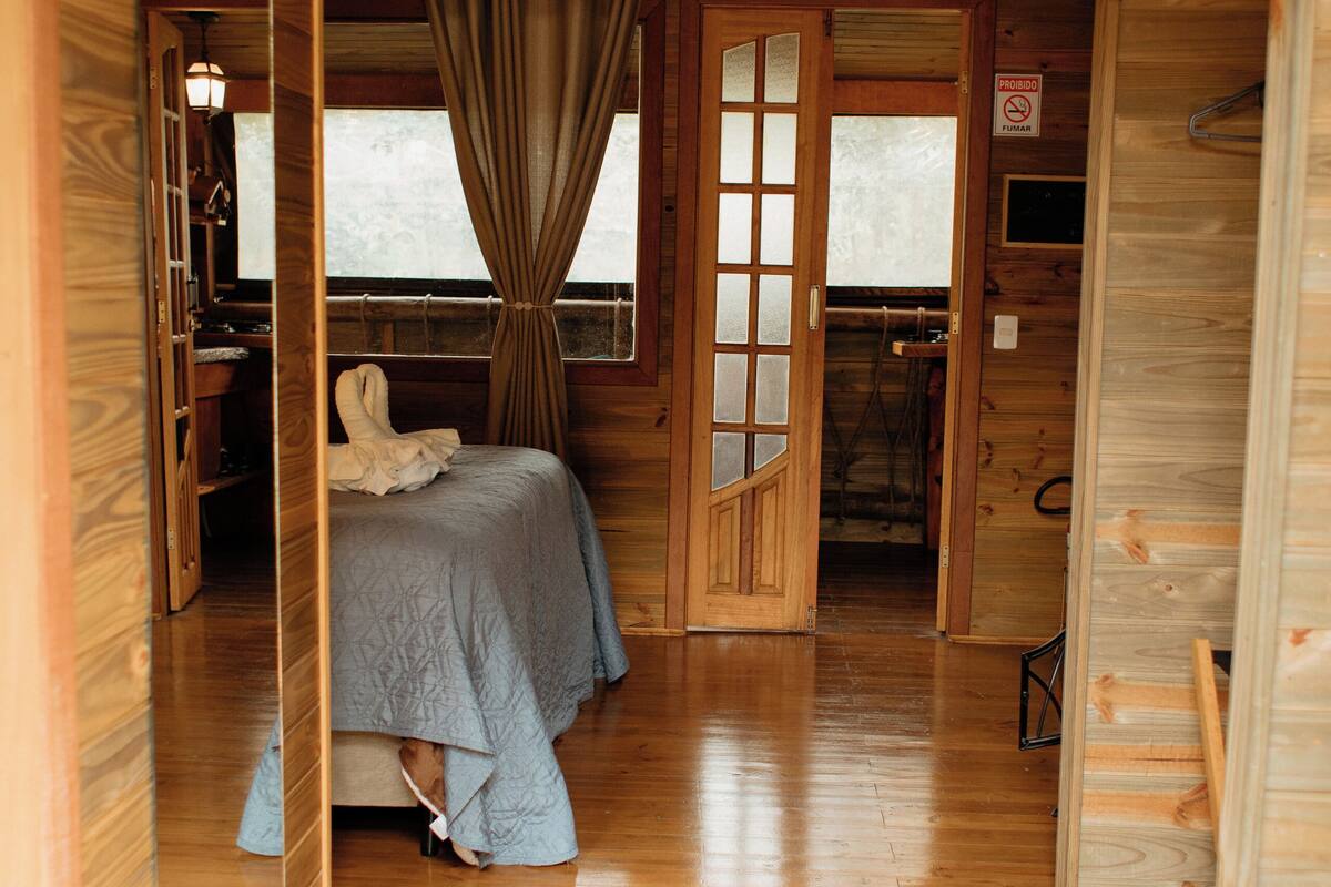 A wooden cabin room with a bed, a desk, and a chair.