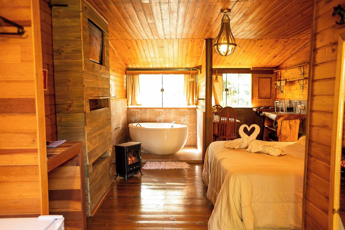 A wooden cabin with a large bathtub, a bed with heart-shaped pillows, and a small table with a book.