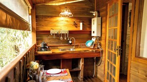 A compact kitchen with wooden walls, a sink, a stove, and a dining area set with plates and cutlery. - Pousada Chalés da Mantiqueira (Campos do Jordão)