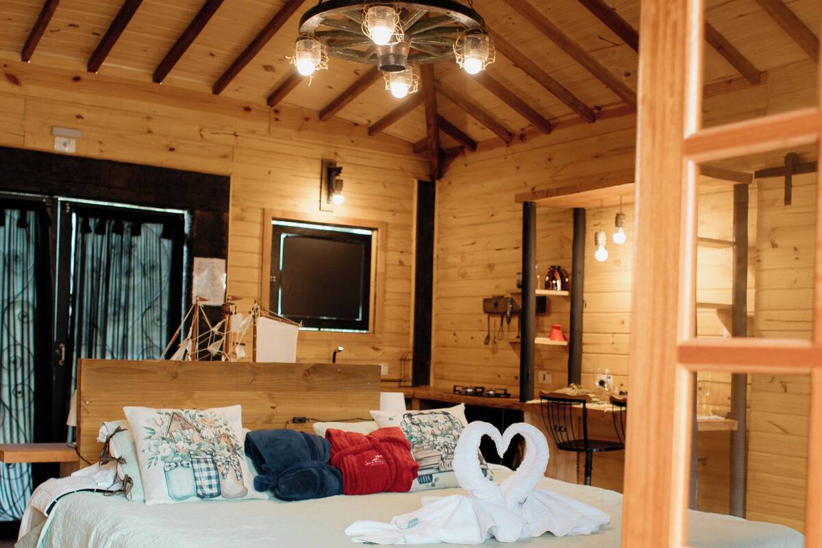 A wooden cabin bedroom with a bed, a desk, and a television.