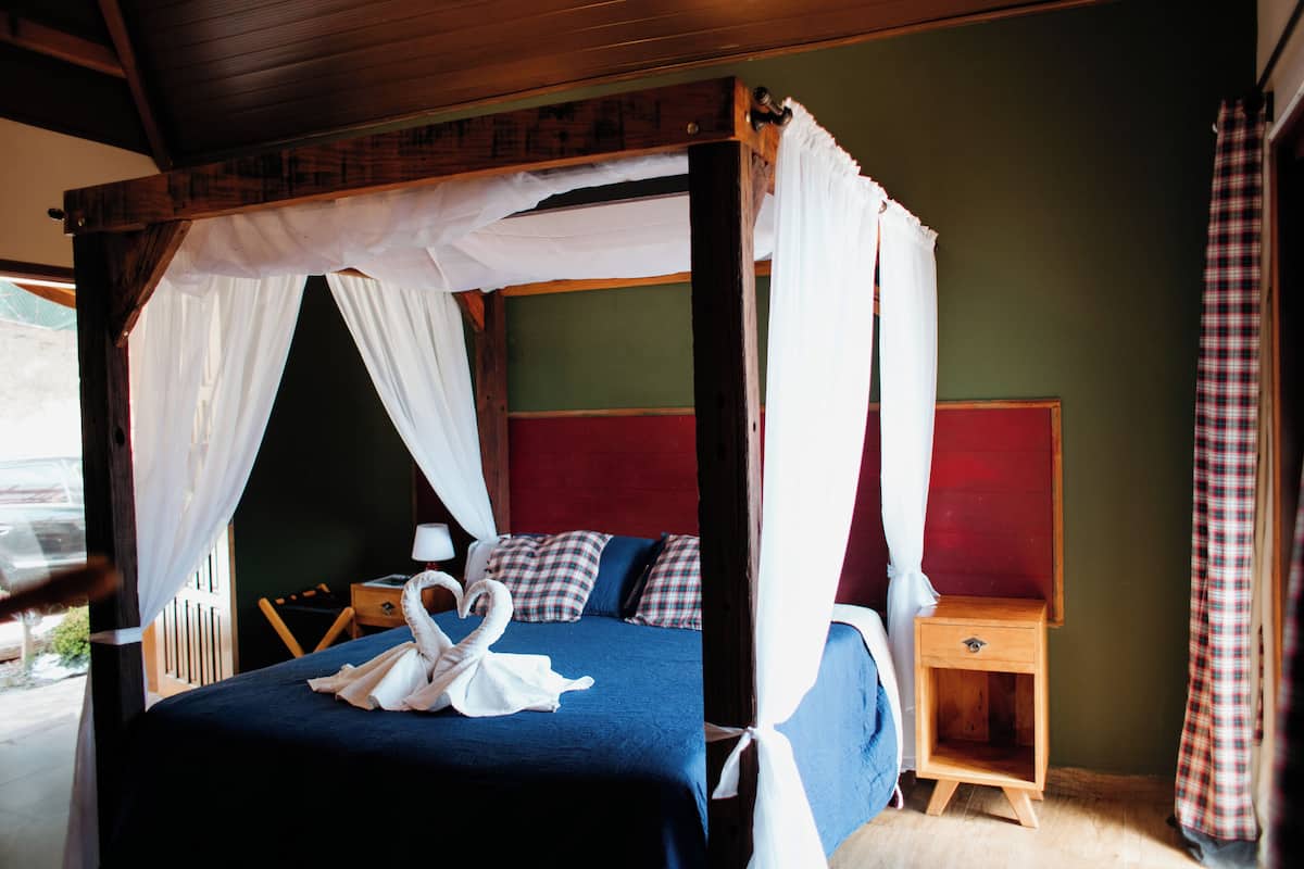 A four-poster canopy bed with a swan-shaped towel, a bedside table, and a red headboard.
