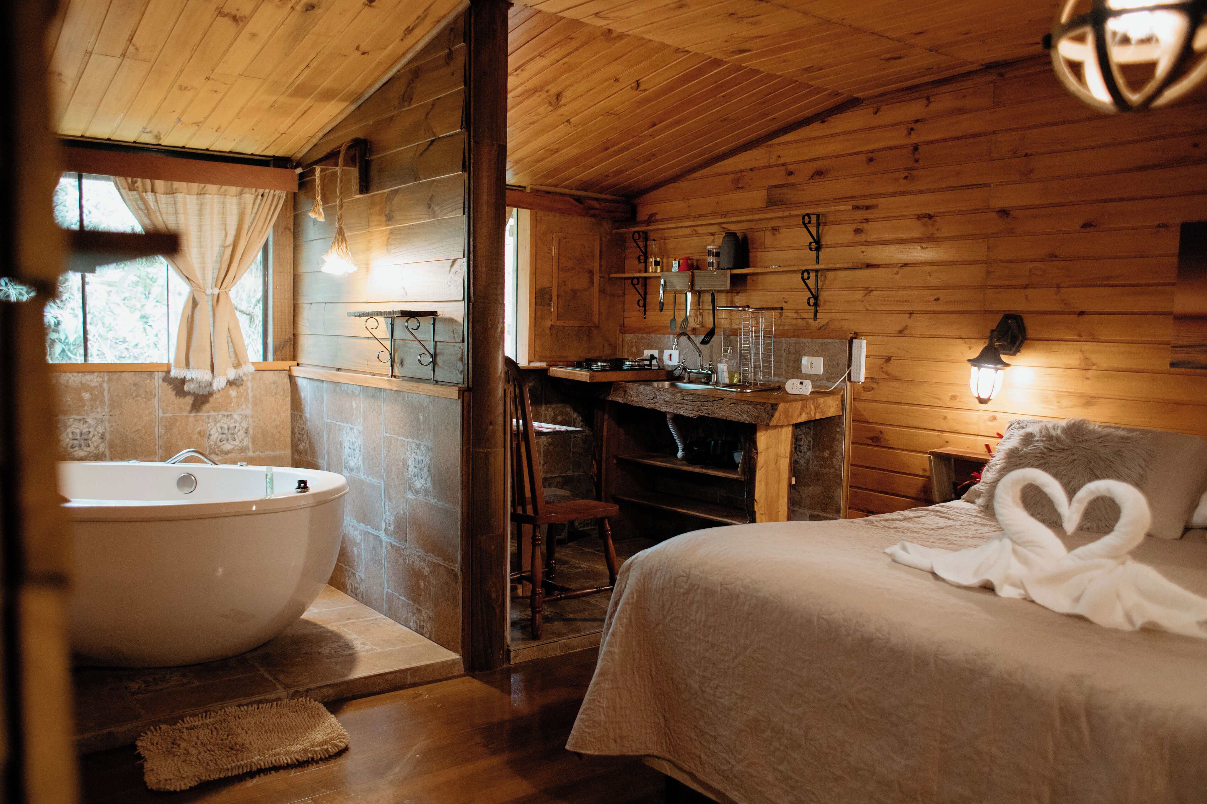 L’intérieur d’un chalet en bois, avec une grande baignoire, un bureau et un lit agrémenté d’une serviette en forme de cœur.
