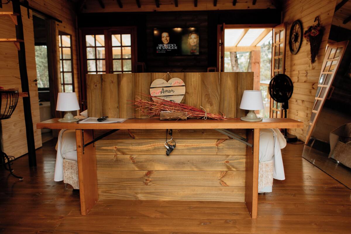 A wooden interior with a central table, two lamps, a heart-shaped decoration, and a television in the background.