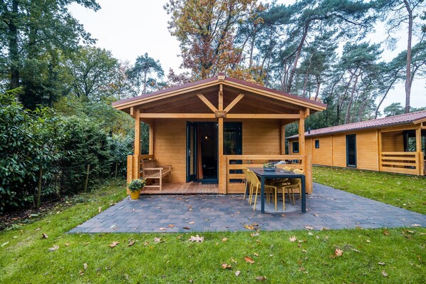 A wooden cabin with a patio, a dining area, and a door leading to the interior.