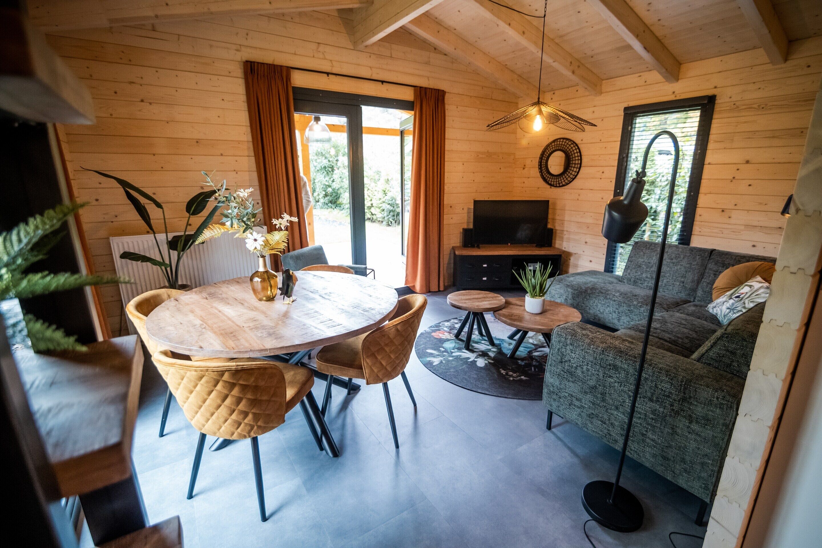 A cozy cabin interior with a wooden dining table, chairs, a sofa, and a TV.