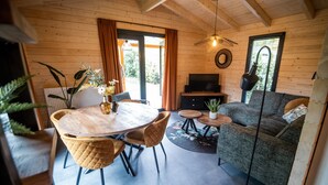 A cozy cabin interior with a wooden dining table, chairs, a sofa, and a TV. - Holiday Home in Markelo Near Forest & Pool (Markelo)