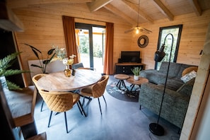 A wooden interior with a dining table, chairs, a sofa, a TV, and a plant.