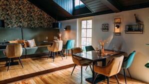 A dining area with a wooden floor, a high ceiling, and a large window. There are chairs and a table with a vase of flowers. - Holiday Home in Markelo Near Forest & Pool (Markelo)