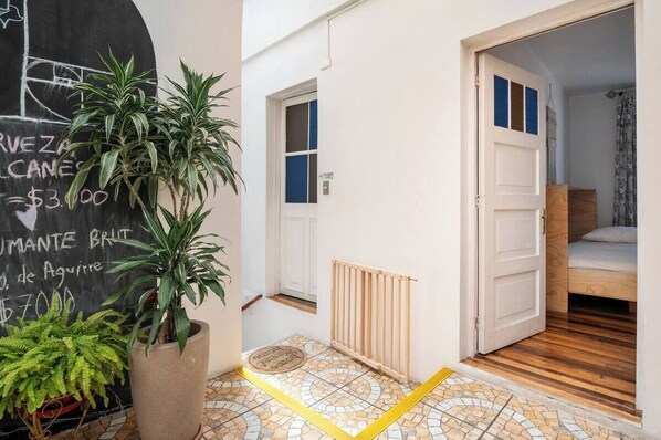 A hallway with a potted plant, a tiled floor, a radiator, and a door leading to a bedroom. - Hostal Casa Fibonacci (Valparaíso)