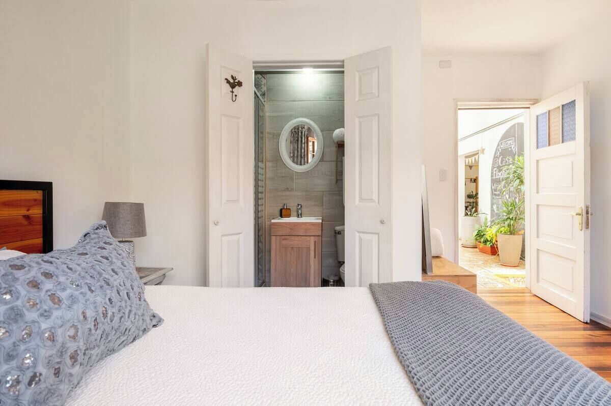 A bedroom with a bed, a nightstand, a lamp, and a view of the bathroom and outdoor area.
