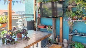 A wooden deck with a table and benches, surrounded by potted plants and a television mounted on the wall. - Hostal Casa Fibonacci (Valparaíso)