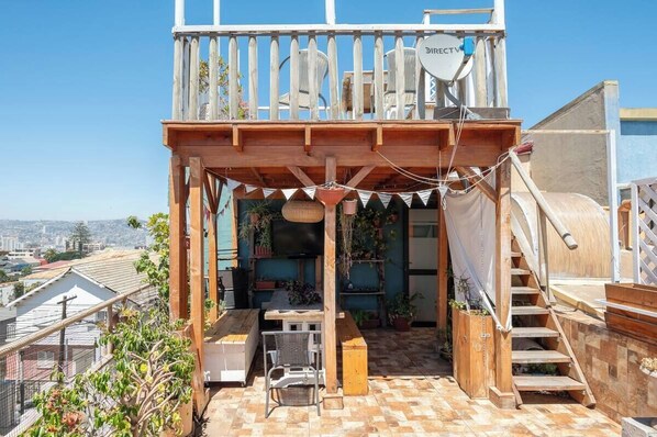 Una terraza en la azotea con una pérgola de madera, mobiliario exterior y una antena parabólica.