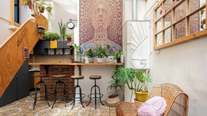 A cozy kitchen with a wooden staircase, a hanging tapestry, and a wicker chair with a cushion. - Hostal Casa Fibonacci (Valparaíso)