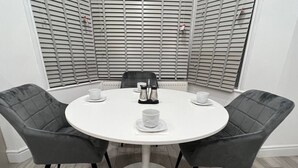 Et rundt bord med fire grå polstrede stole, et hvidt borddække og et sæt hvide kopper og underkopper.