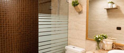 A modern bathroom with a glass shower enclosure, a toilet, a sink with a marble countertop, and a large mirror.