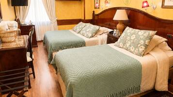 A hotel room with two beds, a desk, a chair, a chandelier, and a patterned rug.