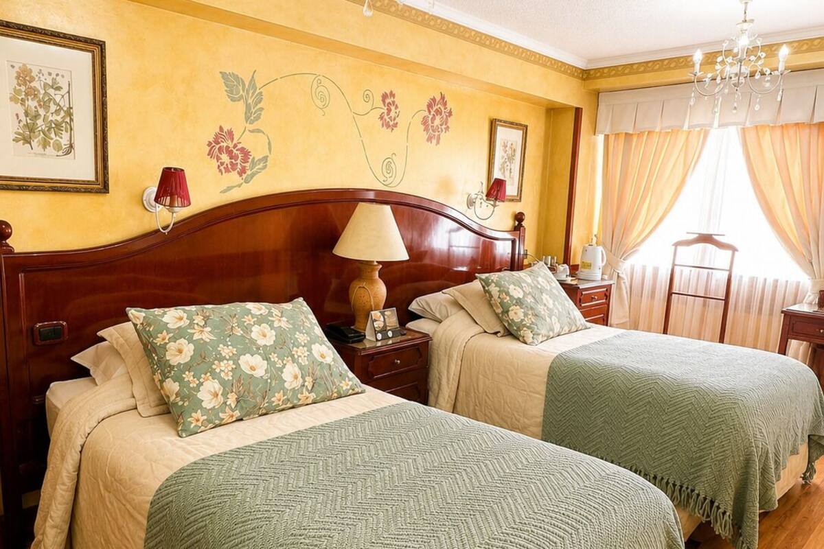 A hotel room with two beds, wooden headboards, a chandelier, and floral wall decorations.