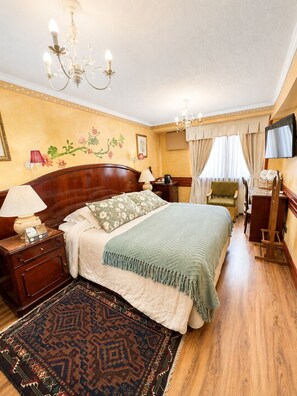 Ein Hotelzimmer mit einem Bett, Nachttischen, einem Chandelier, einem Fernseher und einem Fenster mit Vorhängen.