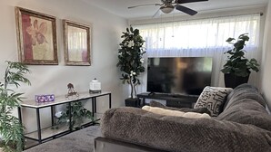 A living room with a sofa, a TV, a ceiling fan, and two potted plants. - Peaceful & Pet Friendly (Gainesville)