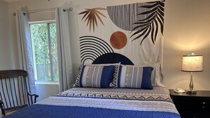 A bedroom with a bed, a nightstand, a chair, and a window with curtains. - Peaceful & Pet Friendly (Gainesville)