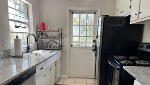 A compact kitchen with white cabinets, a black refrigerator, a stove, and a sink. - Peaceful & Pet Friendly (Gainesville)