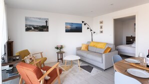 Un salon moderne avec un canapé, des fauteuils, une table à manger dressée pour deux personnes et des œuvres d’art accrochées aux murs.