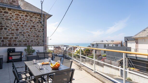 Une terrasse avec un mur en pierre, une table avec des chaises et une vue sur la mer.
